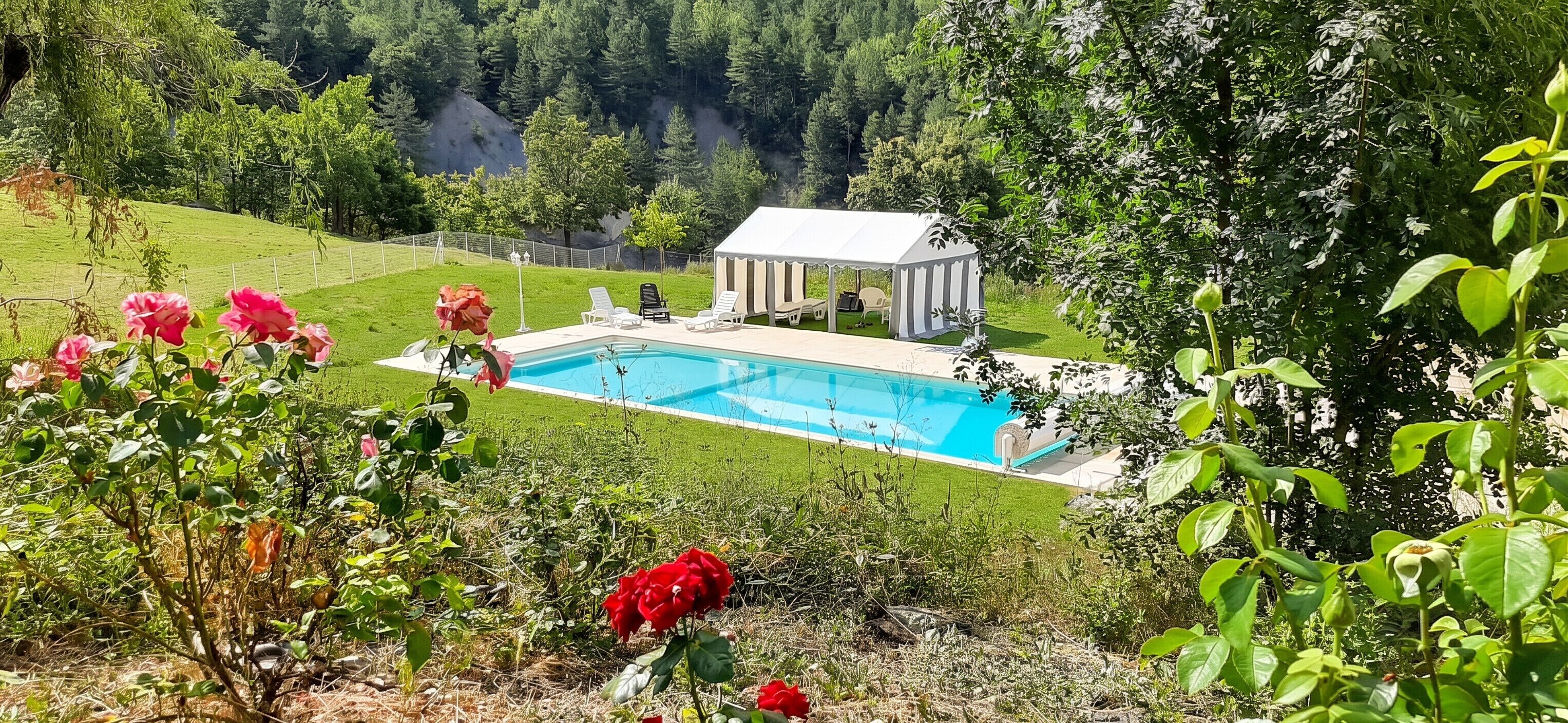 Ein Schwimmbad mit einem Gazebo, umgeben von viel Grün und Hügeln.