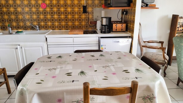 Cuina amb microones, torradora i cafetera, taula de dinar amb cadires i taulells amb rajoles decoratives.