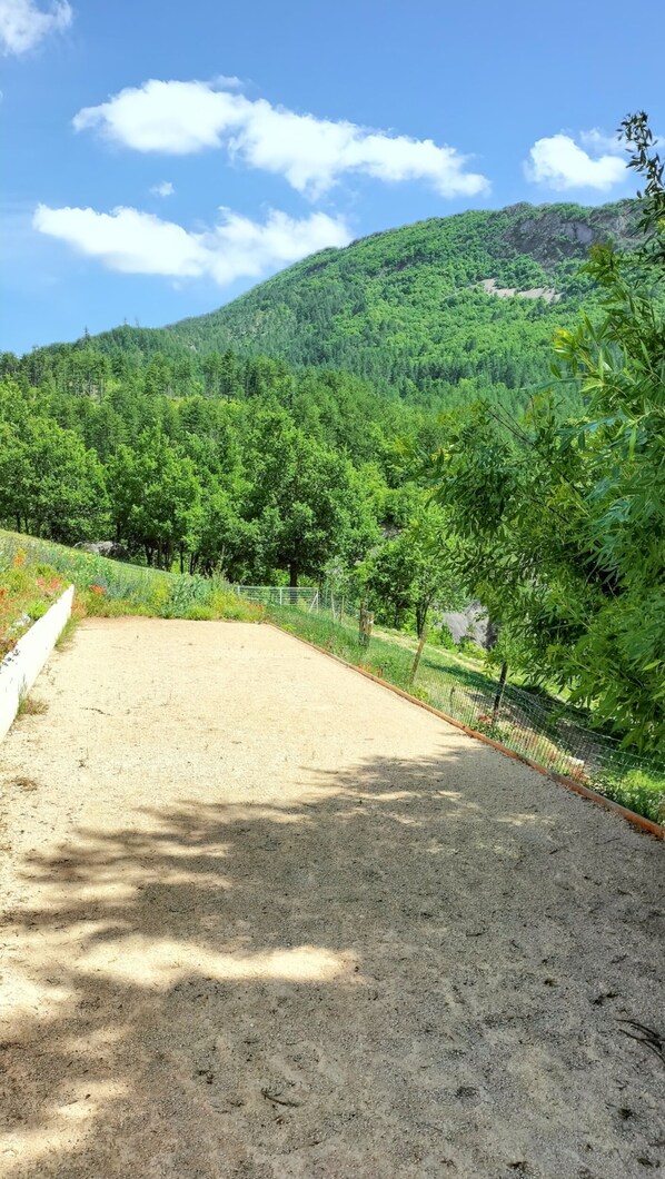 A dirt path leading to a fenced area with a view of a lush green forest and a hill in the background. - Homerez - Villa in Sisteron with Pool (Sisteron)