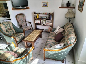 A living room with a sofa, armchairs, a coffee table, a bookshelf, and a television.