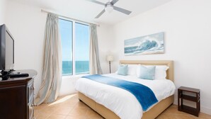 A bedroom with a bed, a TV, a ceiling fan, a lamp, and a window with curtains. - Sapphire 1505 - By GISO Vacation Rentals (South Padre Island)