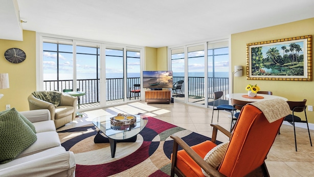 A spacious living room with a large window, a sofa, a coffee table, and a TV. - Direct Beachfront Unit - Shores of Madeira #505 (Madeira Beach)
