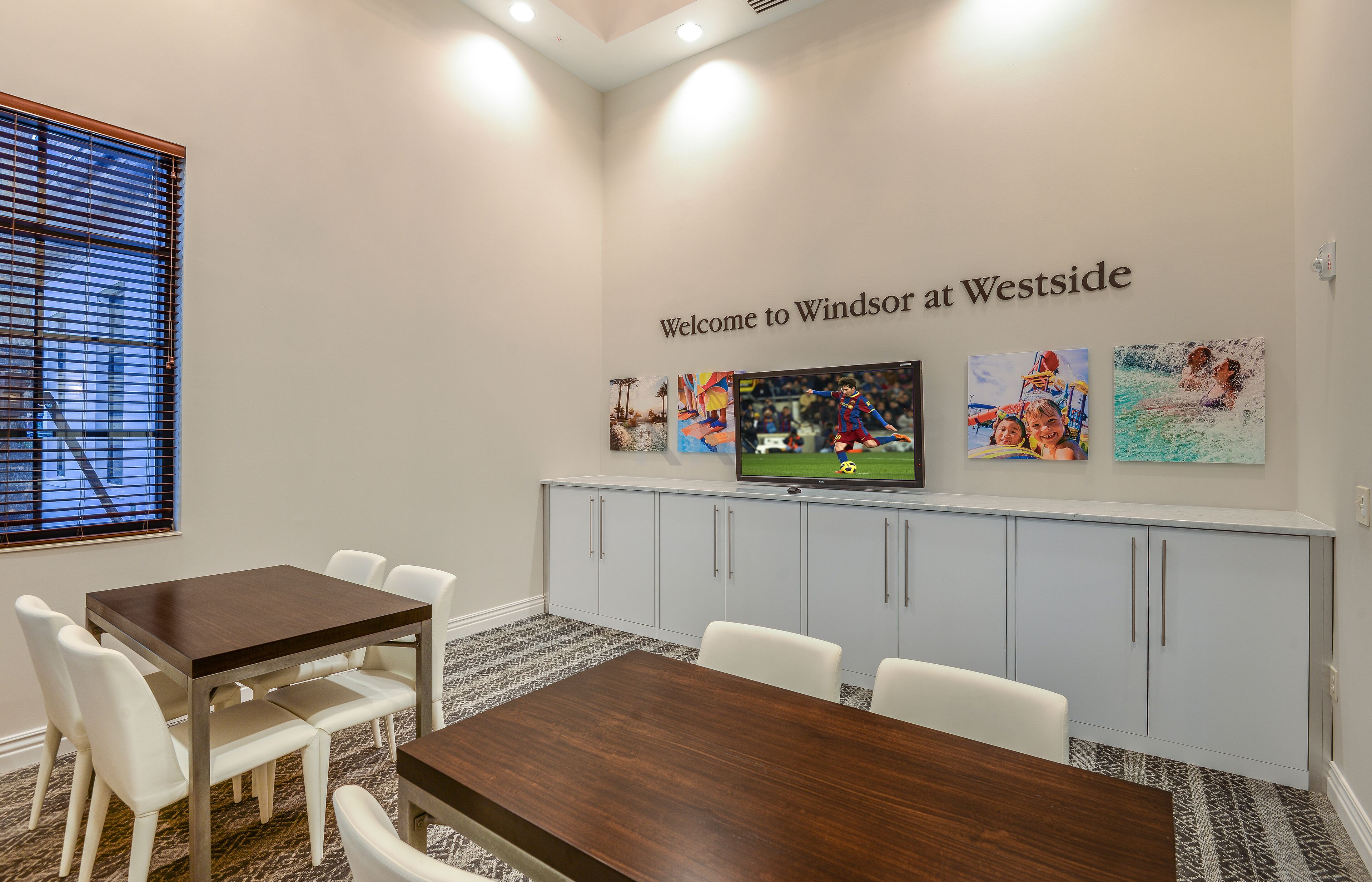 A conference room with a wooden table and white chairs, a television on a stand, and artwork on the wall.