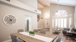 A spacious dining area with a wooden table and grey chairs, a decorative wall piece, and a staircase leading to another level.