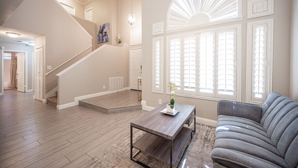 A spacious living area with a wooden floor, a grey sofa, a coffee table, and a staircase leading to another level.