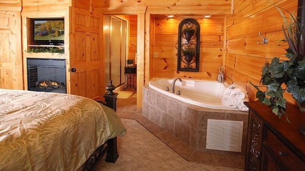 A log cabin bedroom with a large bed, a fireplace, a television, and a bathroom with a bathtub and sink. - Beautiful, clean, comfortable and great views!!  Romantic and family friendly (Sevierville)
