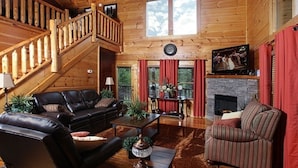 A log cabin interior with a staircase, leather sofas, a fireplace, and a television. - Beautiful, clean, comfortable and great views!!  Romantic and family friendly (Sevierville)
