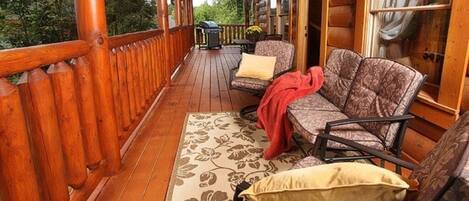 A wooden deck with a sofa and chairs, a grill, and a window with curtains.