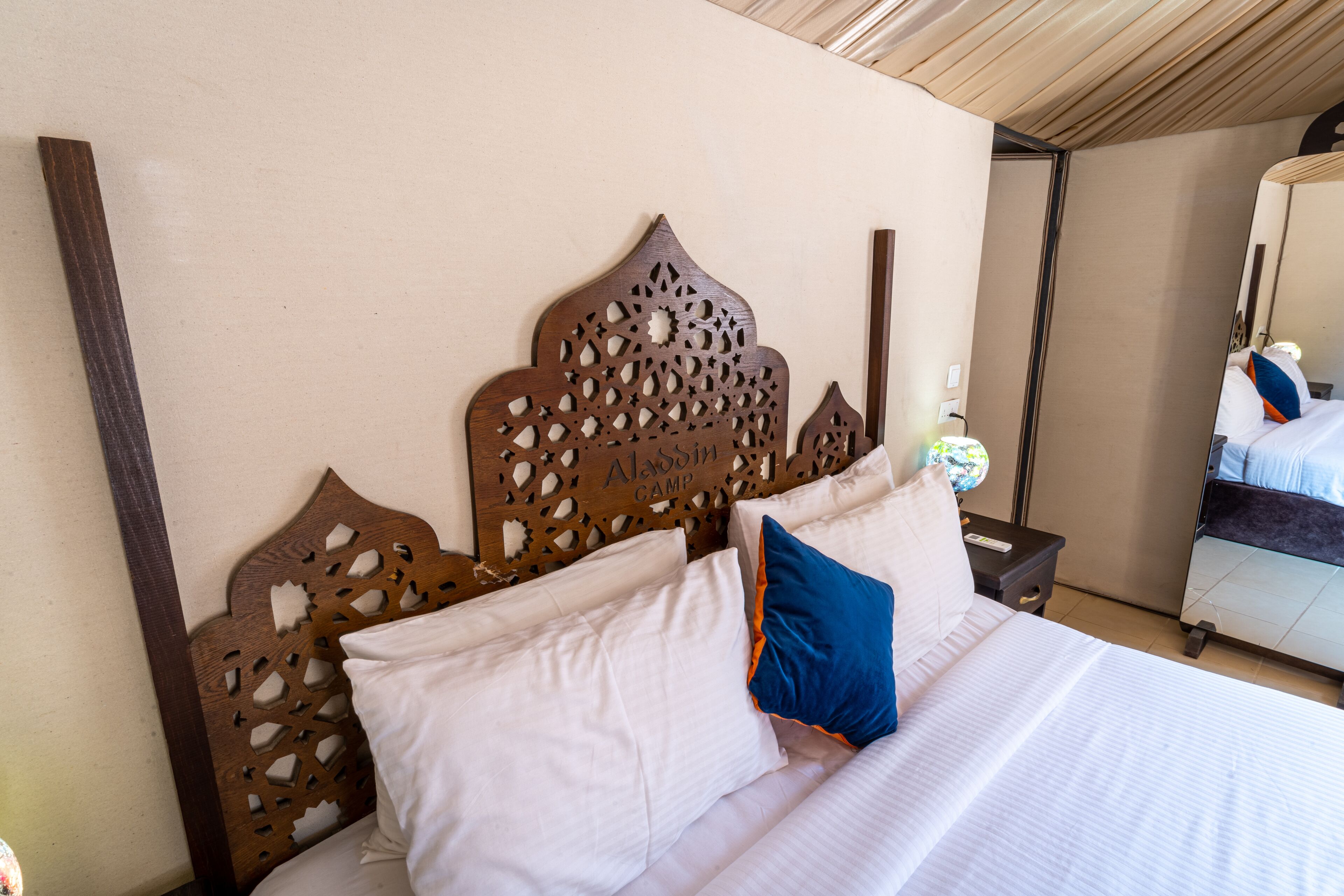 A hotel room with a bed, a wooden headboard, and a nightstand with a lamp.