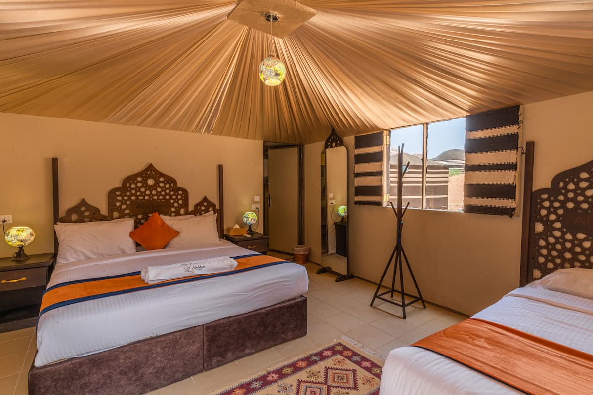 A bedroom with a large bed, a bedside table, a mirror, and a view of the outdoors.