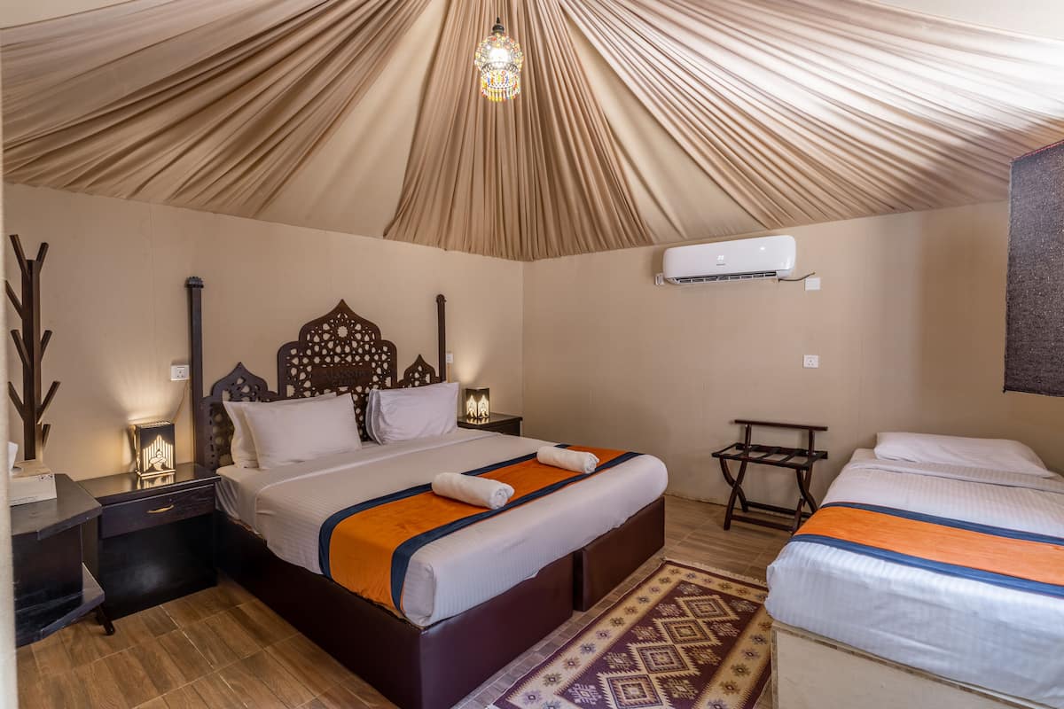 A room with a large bed, a smaller bed, a nightstand, a lamp, and a ceiling fan.