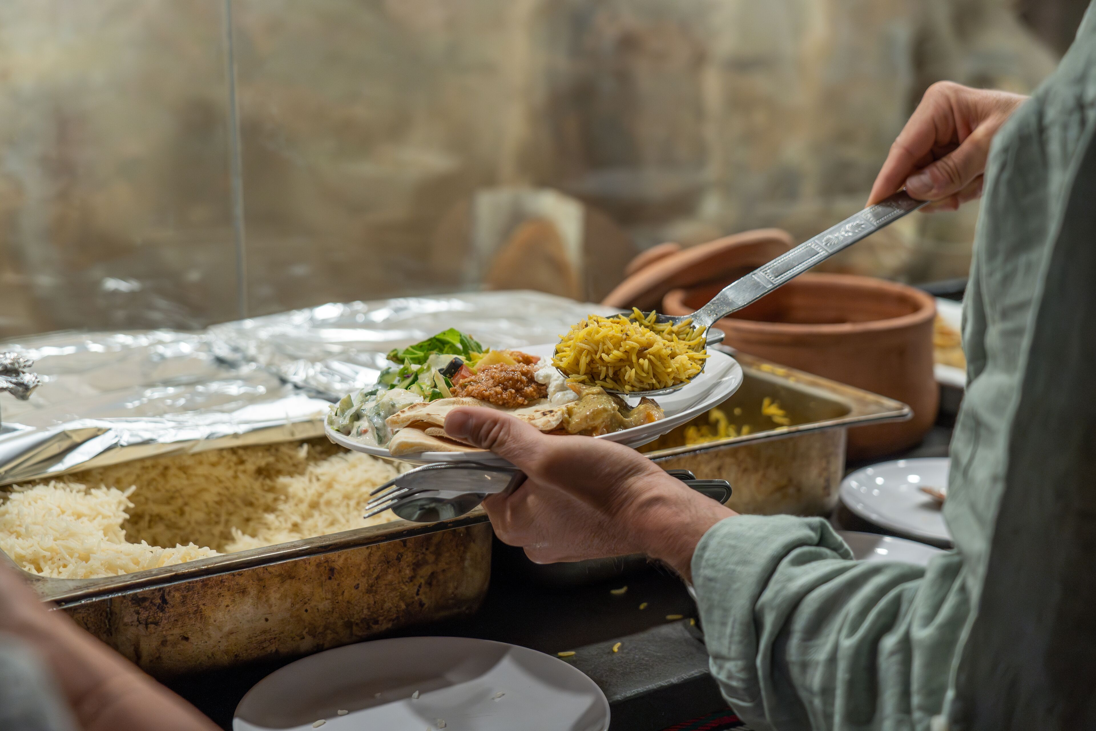 A person serving themselves food from a communal dish, with various dishes visible on the table.