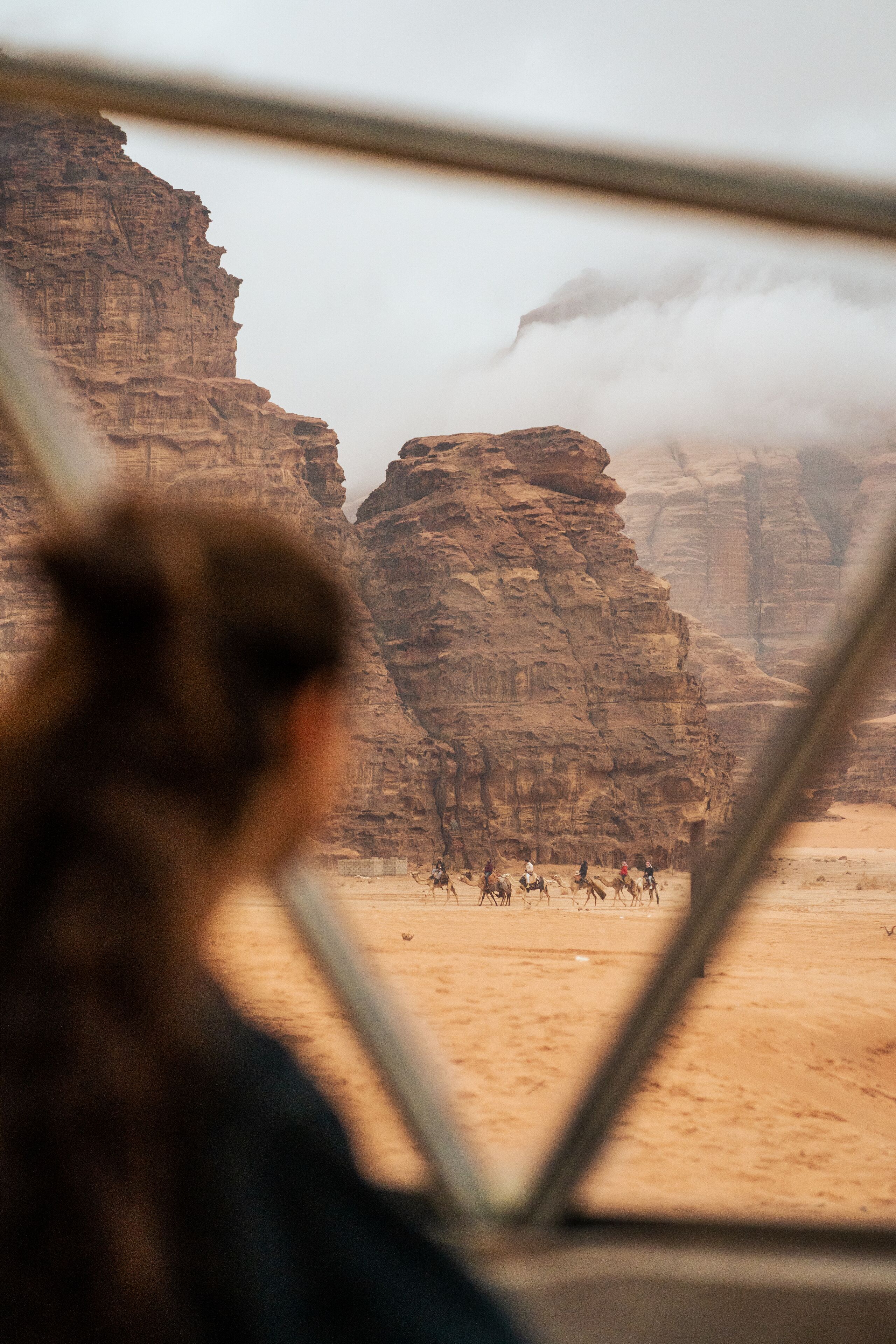 A view from a window of a desert landscape with rocky formations and a group of people riding camels.