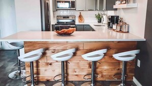 Una cocina moderna con una isla central, taburetes de bar, electrodomésticos de acero inoxidable e iluminación colgante.