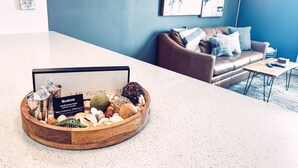 Una zona de recepción con un tazón de madera con objetos decorativos, un mostrador blanco, un sofá de cuero marrón y una pared azul con cuadros enmarcados.
