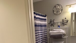 Une salle de bain avec un rideau de douche à rayures, des toilettes, une étagère avec des serviettes pliées et une poubelle.