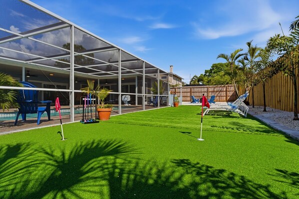 A backyard with artificial grass, a pool, and a covered patio area.