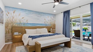 A bedroom with a bed, nightstands, a ceiling fan, and a view of a swimming pool through a glass door.