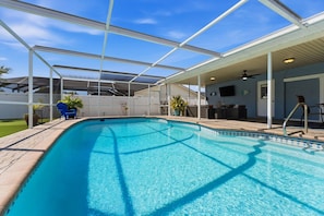 A covered swimming pool with a glass ceiling, a ceiling fan, and a television on the wall.