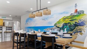 A dining area with a table set for six, chairs, and a mural of a lighthouse on the wall.