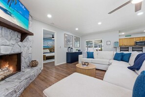 A modern living room with a stone fireplace, a white sofa, a round coffee table, and a kitchen area in the background.