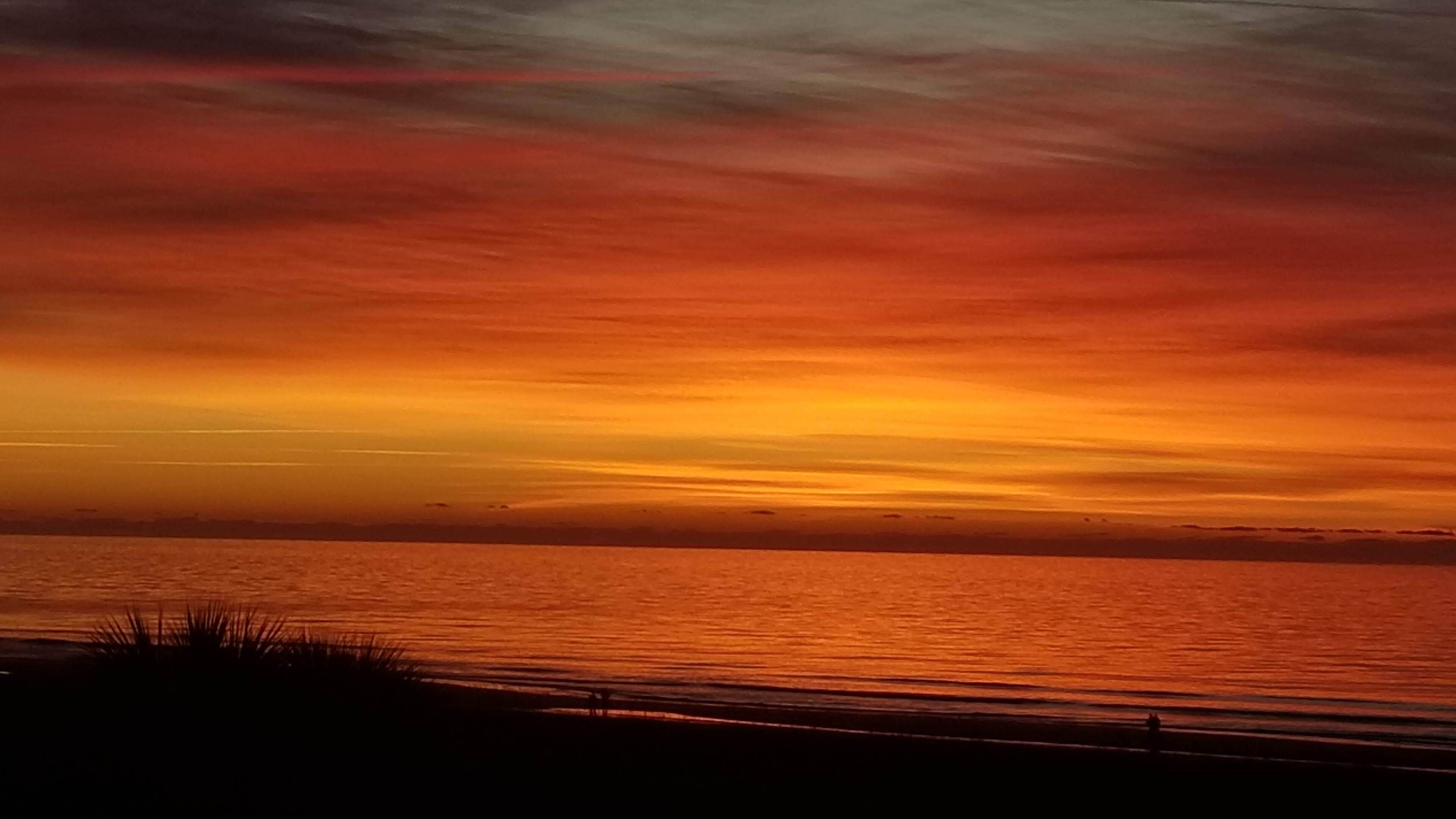 A sunset over a calm sea with a silhouette of a beach in the foreground.