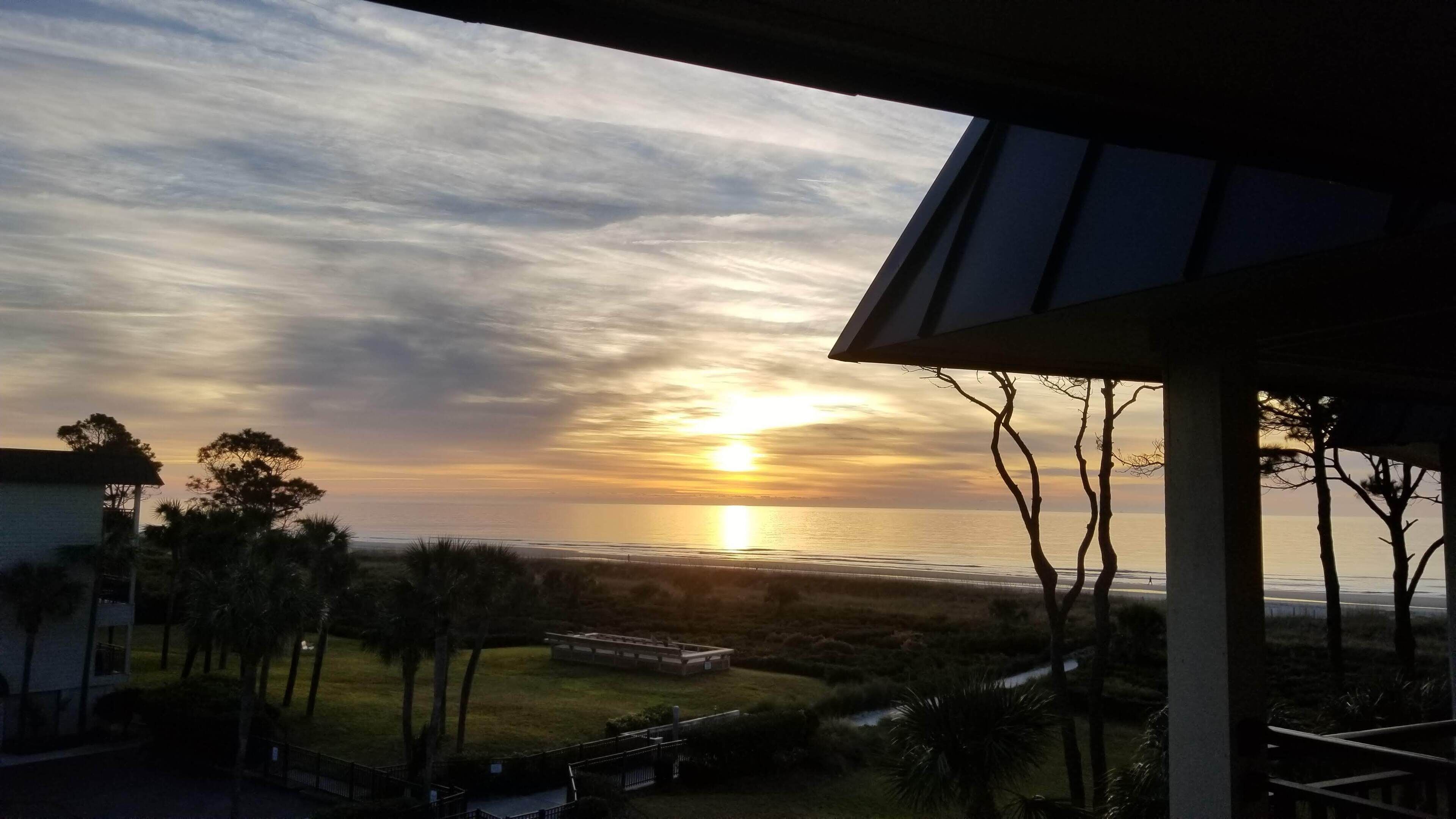 A sunset view from a covered outdoor area with a view of the ocean and a grassy landscape.