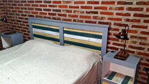 A bed with a striped headboard, two bedside tables, and a brick wall background. - La Maina Uribe Posada y Cabañas (Lobos)