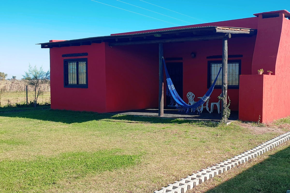 A red building with a porch, a hammock, and a small garden area.