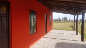 A red building with a covered porch and a view of a grassy field. - La Maina Uribe Posada y Cabañas (Lobos)
