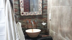 A bathroom with a stone wall, a mirror with a mosaic frame, a sink, and a towel rack. - La Maina Uribe Posada y Cabañas (Lobos)