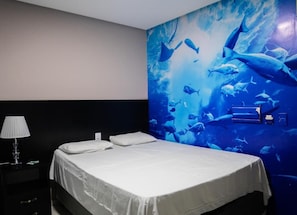 Ein Hotelzimmer mit Bett, Nachttisch, Lampe und Wandgemälde einer Unterwasserlandschaft.