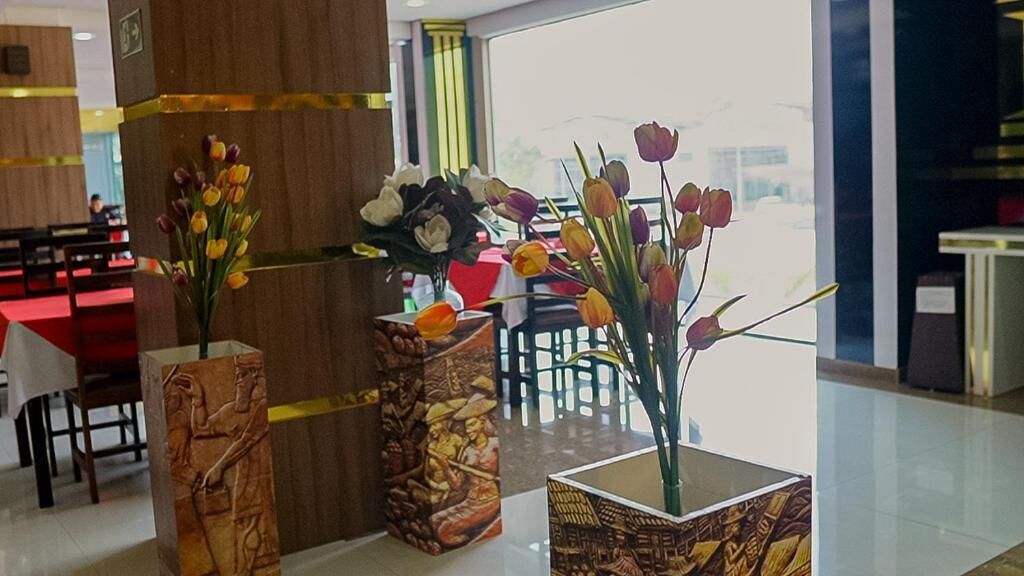 Un hall de hotel con mostrador de recepción, zona de estar y jarrones decorativos con flores.
