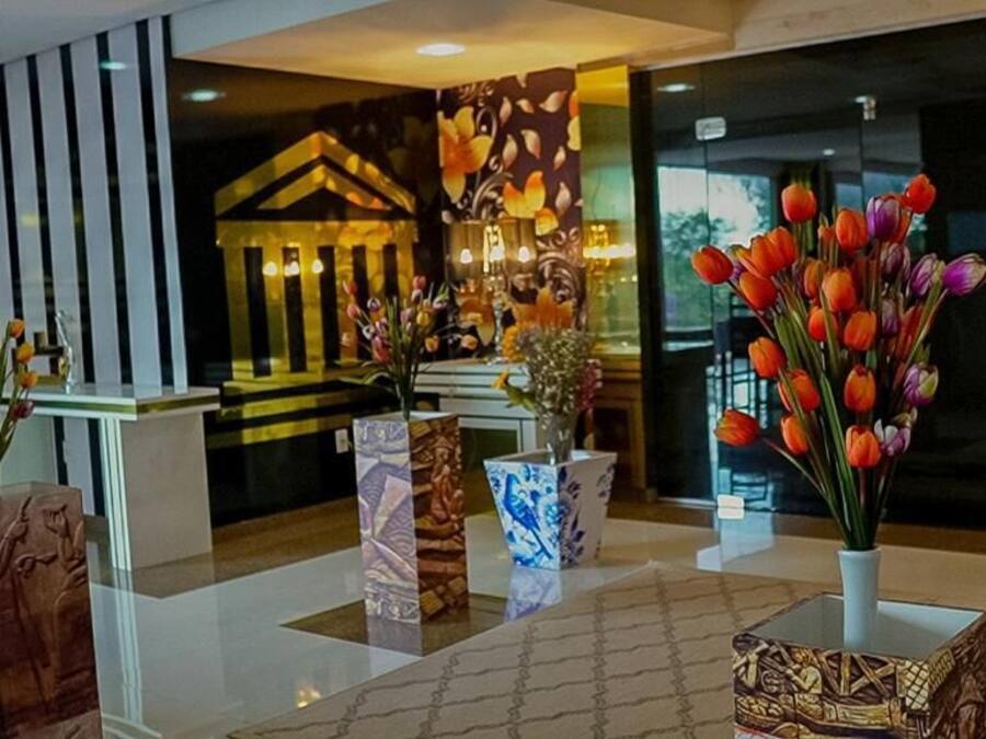 Zona de recepción con diseño moderno, que incluye un mostrador de recepción, jarrones decorativos con flores y un suelo con estampado.