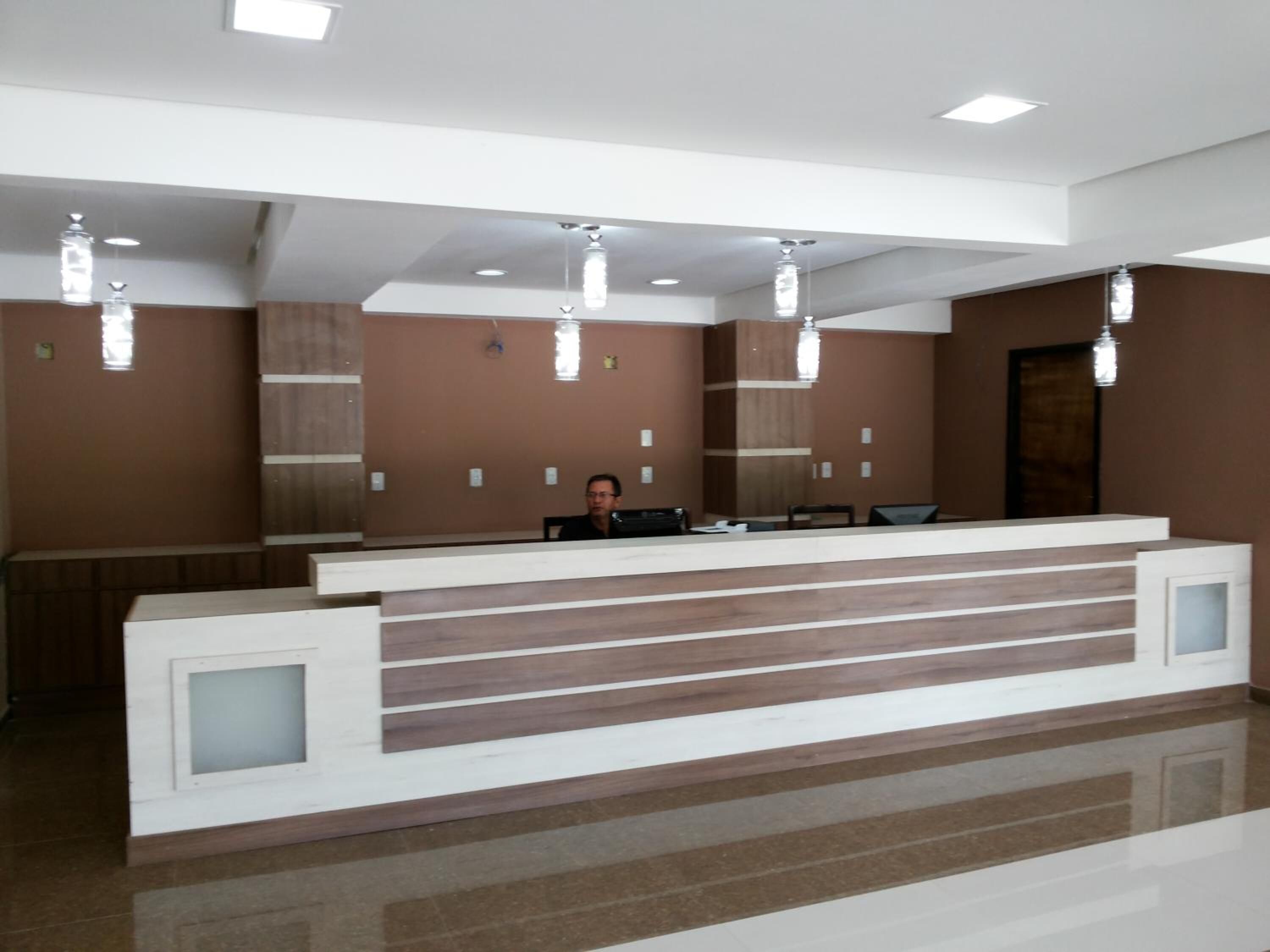 Un mostrador de recepción moderno con una persona sentada detrás, un espejo grande e iluminación empotrada en el techo.