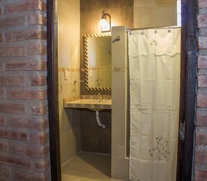 A bathroom with a tiled floor, a sink with a mirror, and a shower curtain.