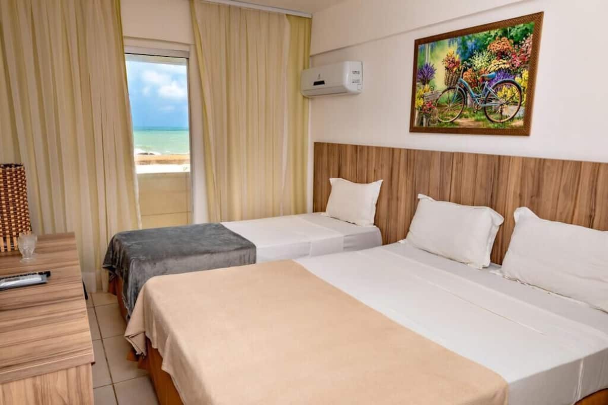 A hotel room with two beds, a wooden desk, an air conditioning unit, and a painting of a bicycle on the wall.