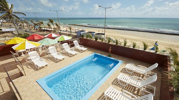 A pool area with lounge chairs and umbrellas, overlooking a beach. - Brisa do Mar Beach Hotel (Natal)