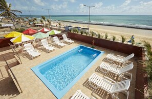 A pool area with lounge chairs and umbrellas, overlooking a beach. - Brisa do Mar Beach Hotel (Natal)