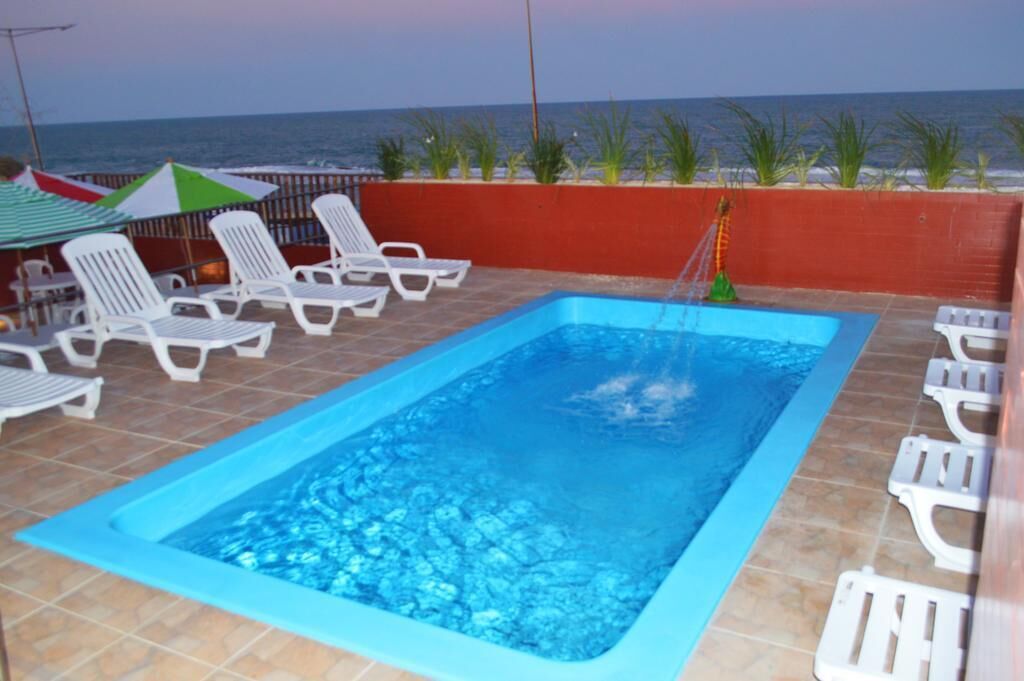 A rectangular swimming pool with a blue border, surrounded by white lounge chairs and a red wall.