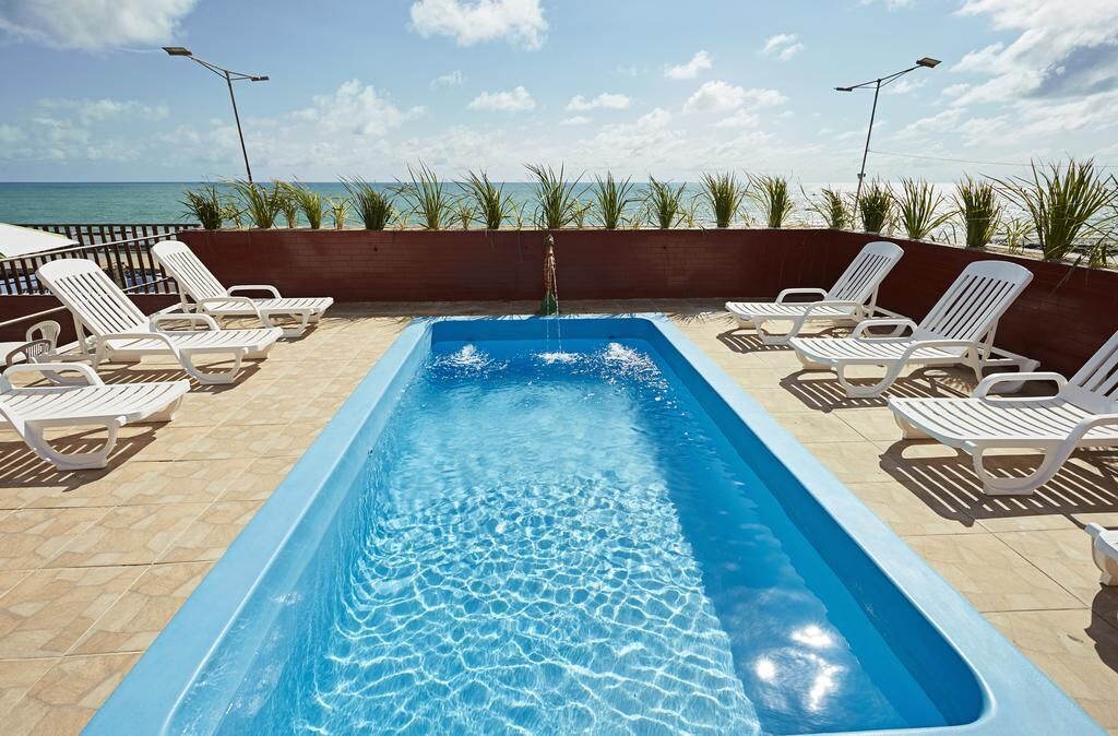 Une piscine rectangulaire à l’eau d’un bleu cristallin, entourée de chaises longues blanches et d’une terrasse en bois.