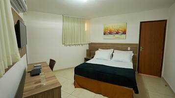 Una habitación de hotel con una cama, un escritorio con computadora, un televisor y un cuadro en la pared.