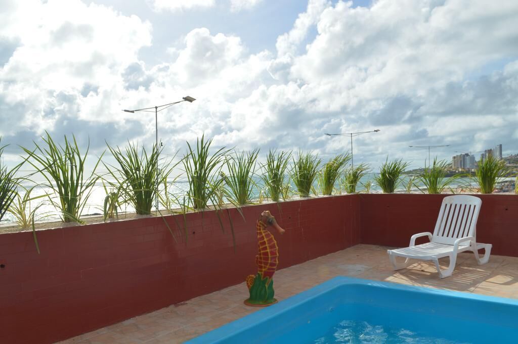 Un espace piscine aménagé sur le toit, agrémenté d’une décoration représentant un hippocampe, d’un fauteuil de relaxation blanc et offrant une vue sur le panorama urbain.