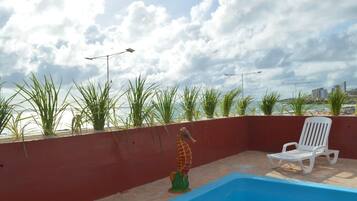 Un espace piscine aménagé sur le toit, agrémenté d’une décoration représentant un hippocampe, d’un fauteuil de relaxation blanc et offrant une vue sur le panorama urbain.