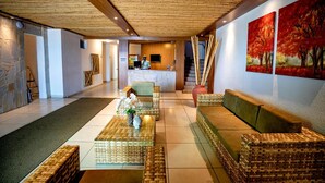 A lobby with a reception desk, wicker furniture, and a large painting of trees. - Brisa do Mar Beach Hotel (Natal)