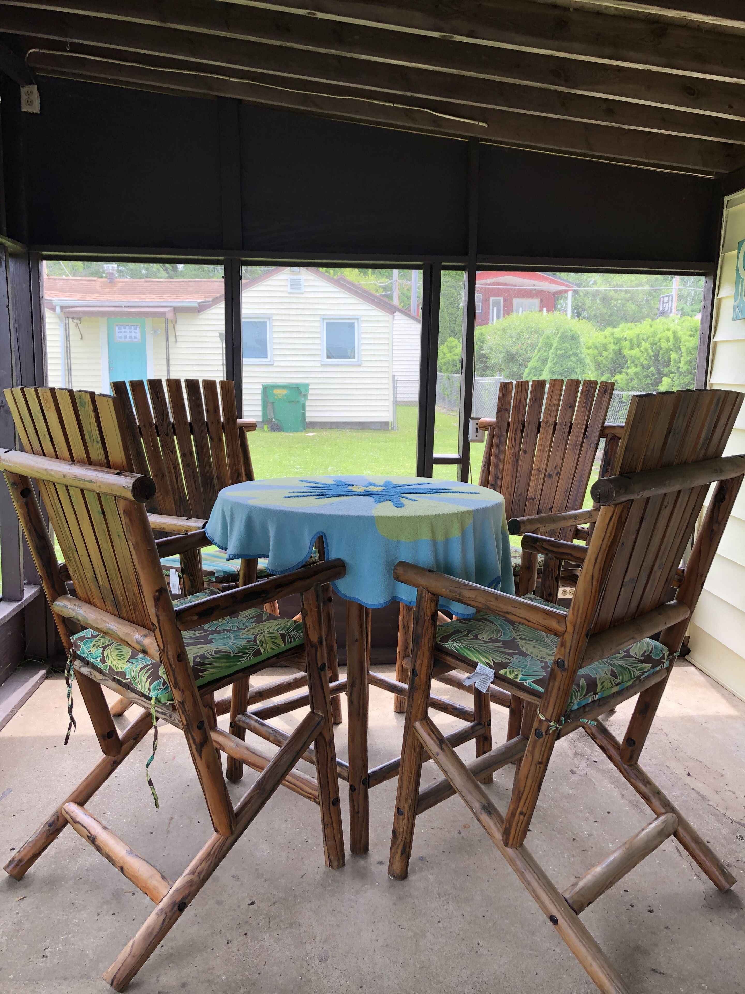A covered patio area with a round table and six wooden chairs with green cushions.