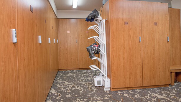 Habitación de hotel con armarios de madera, un estante blanco con bolsos y suelo alfombrado.