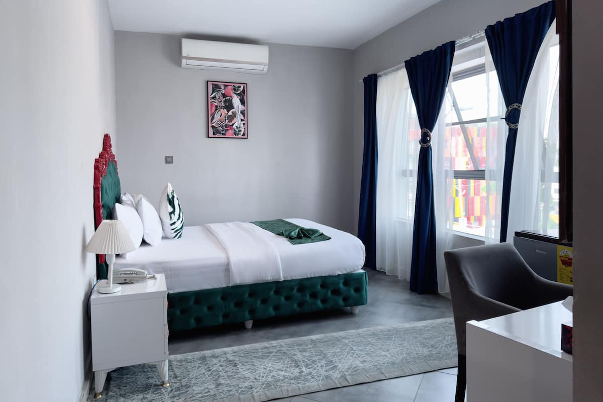 A modern hotel room with a bed, a bedside table, a lamp, a chair, and a window with curtains.