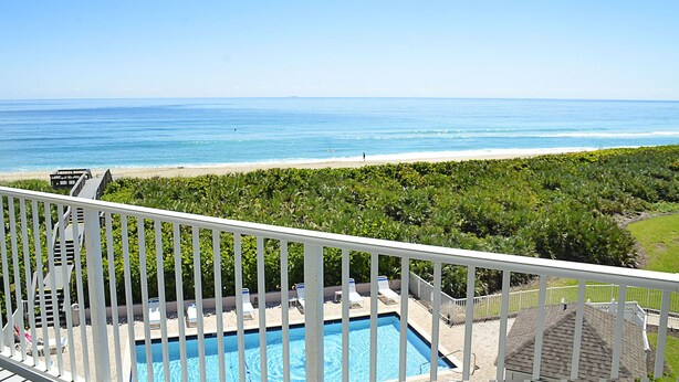 Ein Pool mit Liegestühlen, Blick auf den Strand und einem klaren Himmel.