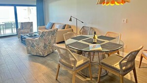 Ein modernes Wohnzimmer mit rundem Glastisch, Korbstühlen, einer Couch und einem Deckenventilator.